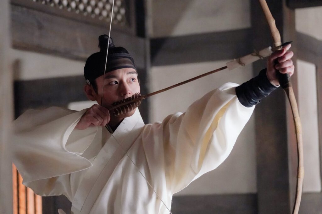 Actor Park Ji-hoon in full royal costume as teenage King Danjong, drawing back a traditional Korean bow. Official promotional still from the film The King's Warden (2026).