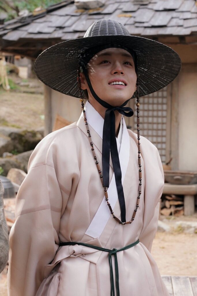 Evolution of Korean traditional hat Gat across Joseon Dynasty and Actor Park Ji-hoon wearing traditional hanbok, smiling warmly as he portrays teenage King Danjong. Official promotional still from the film The King's Warden (2026).